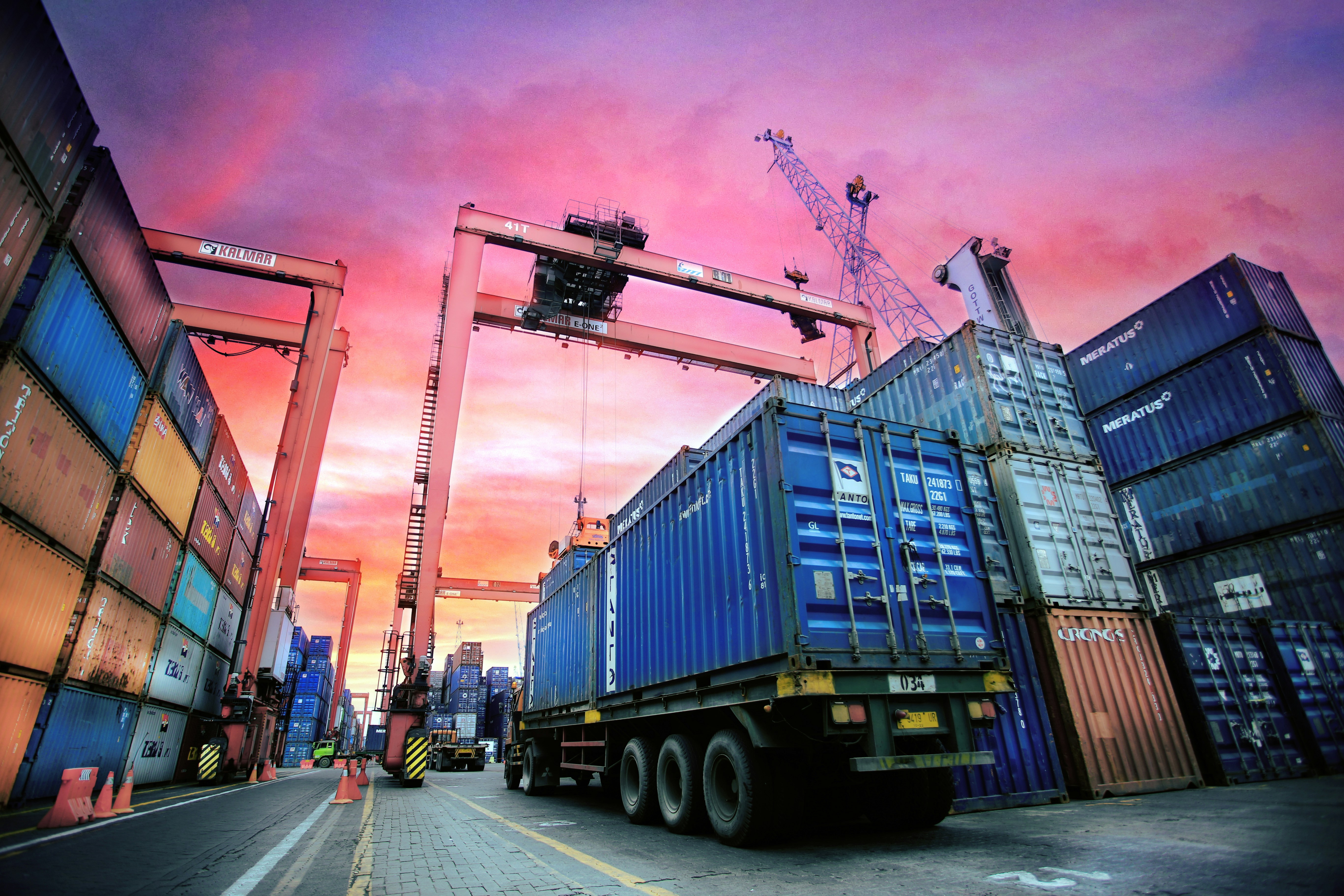 Truck passing under a quay crane while transporting shipping containers in a port, showcasing container transport and port logistics operations.