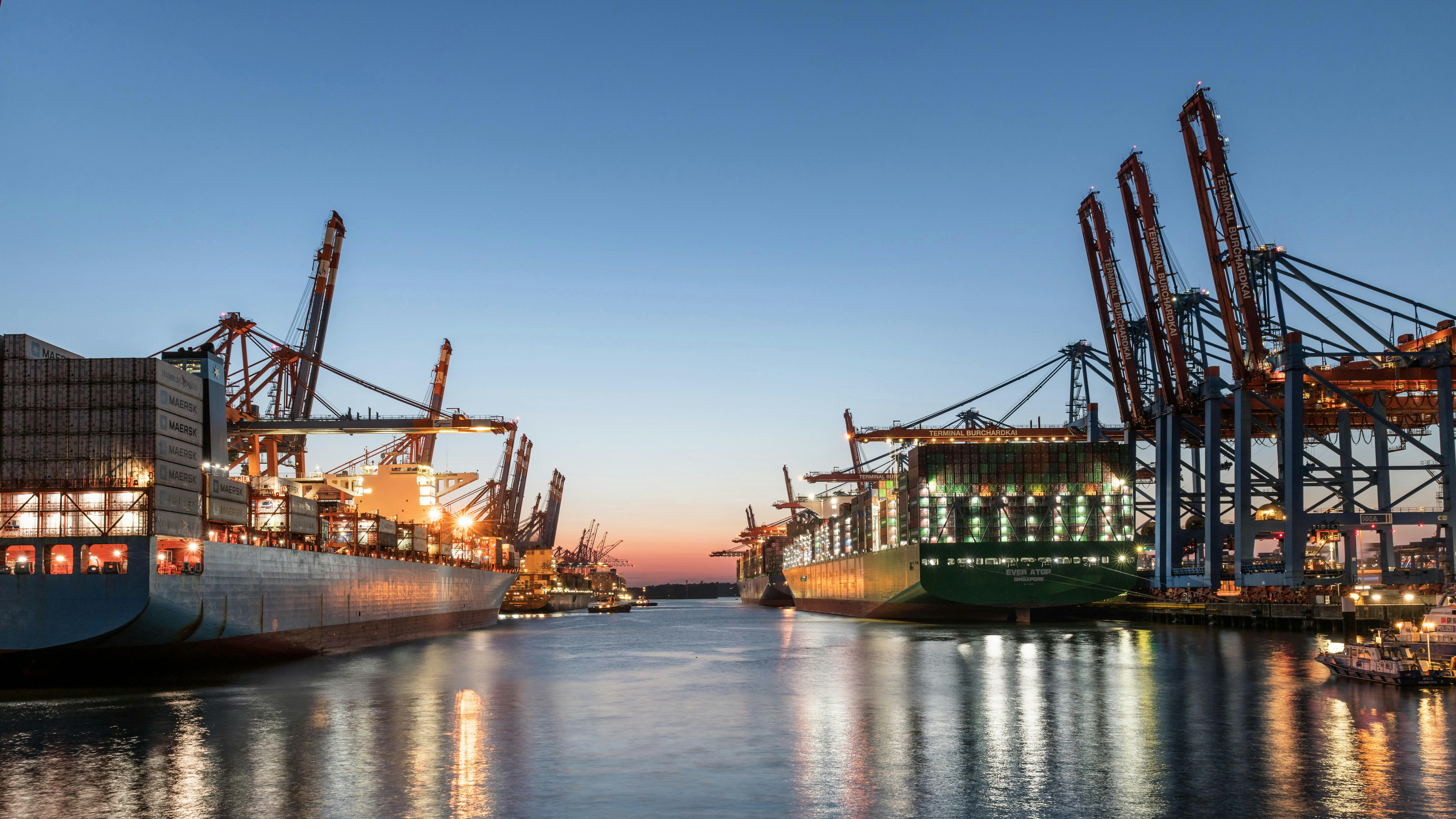 Hamburg container terminal with large vessels carrying stacked containers at the berth, ready for transport, alongside quay cranes by the sea.