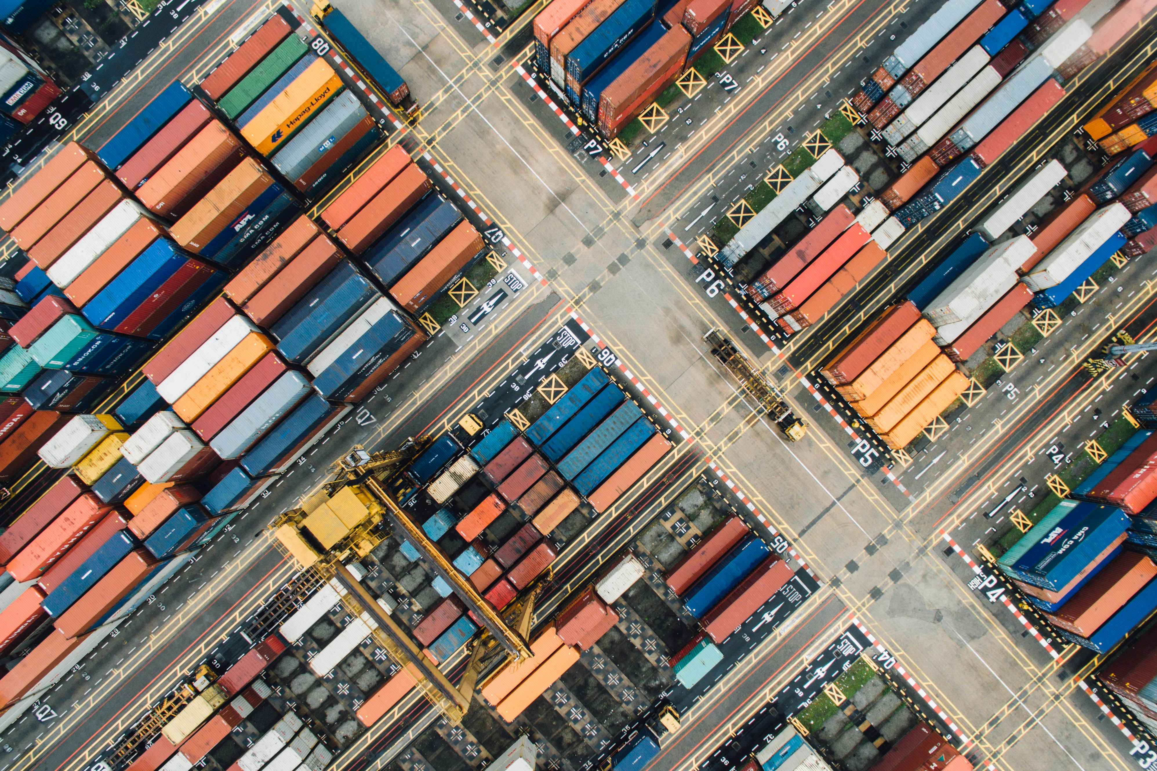 Aerial view of a busy container yard with stacked shipping containers and a traditional diesel truck transporting cargo, representing port logistics operations.